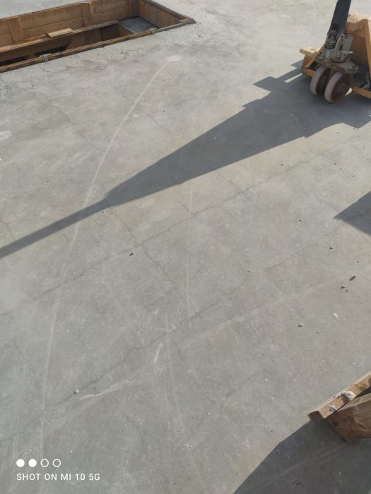 Rektangulära armeringsjärn på en betonggolv med en gaffeltruck i bakgrunden.