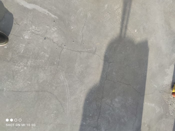 Rektangulära former som möjligtvis är armering syns på en betongyta med en skugga.