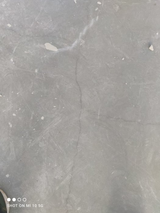 Grå rektangulär stenskiva med synlig spricka och små märken, med skons spets synlig nedtill.