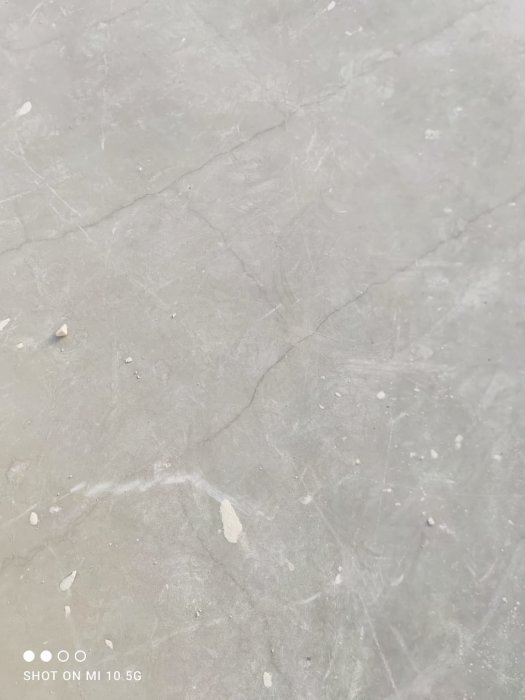 Närbild på en betongyta med sprickor och små stenar, rektangelformade armeringsmönster syns svagt.