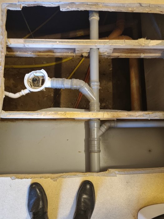 Upprivet golv med synliga avloppsrör och bjälklag, indikation på renovering eller skadedokumentation.