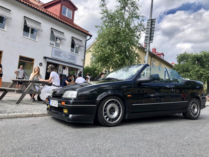 Svart Renault 19 16v cabriolet byggd av Karmann, parkerad på gata med personer i bakgrunden.