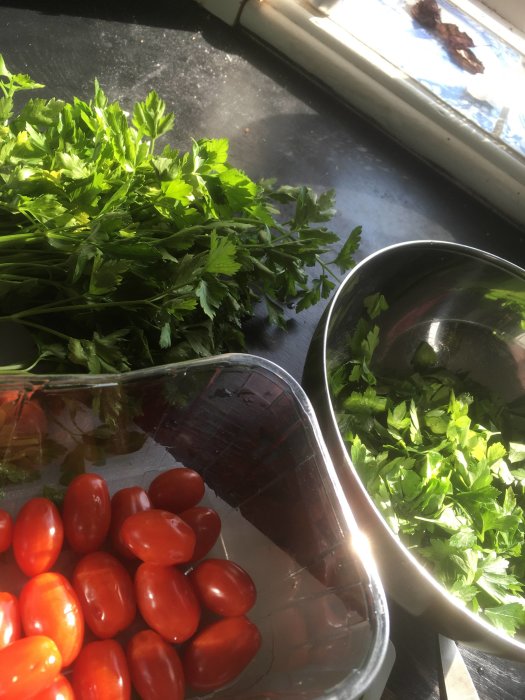 Ingredienser för Tabbouleh: persilja, cocktailtomater och hackad persilja i skål vid fönster.