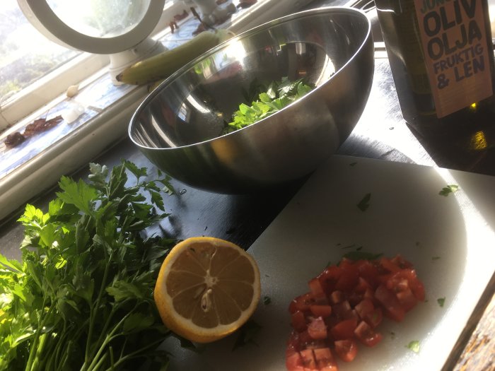 Förberedelse av ingredienser för Tabbouleh: hackade tomater, persilja och citron på skärbräda med skål och olivolja i bakgrunden.