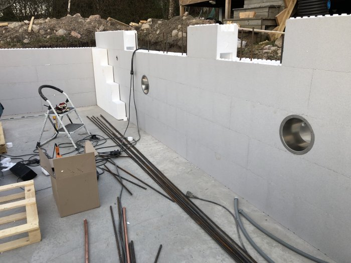 Nybyggnation av en vit betonggrund med fyra lager block och byggmaterial runtomkring.