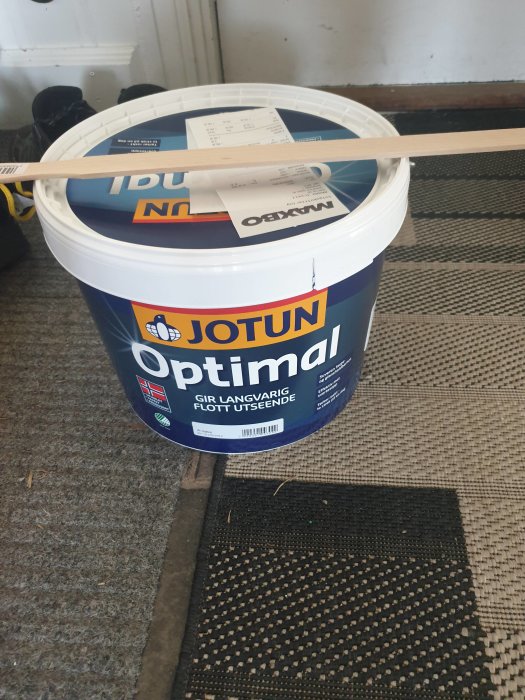 Hink med Jotun Optimal färg och en träremsa på ett rutigt golv inomhus, förberedelse för målning.