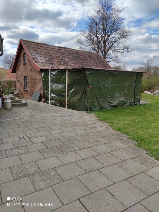 Hus med röda takpannor och tillfällig presenning över carport under ombyggnad.