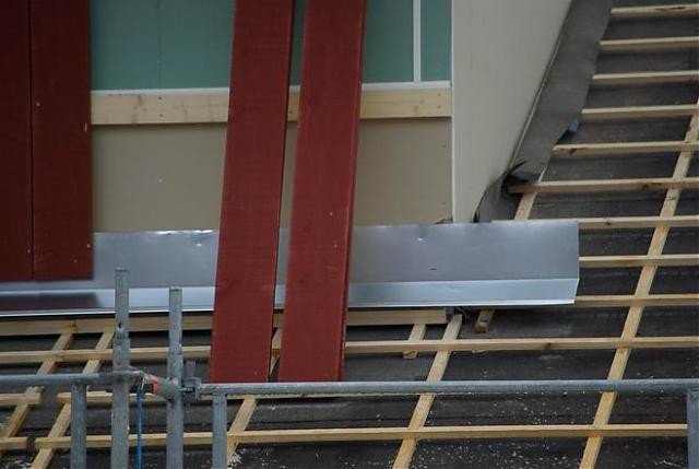 Installation av ett bleck under takpannorna och ovanför ytterpanelen på en husvägg under konstruktion.