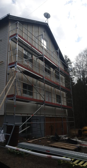 Husfasad med uppställt byggnadsställning, oavslutad arbete på högre delen.