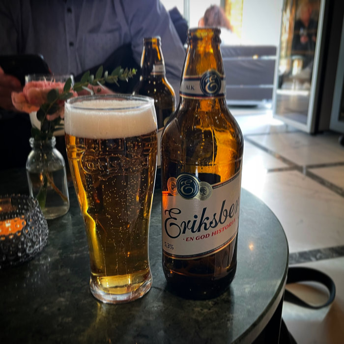 Ett glas fyllt med öl och en ölflaska märkt 'Eriksberg' på ett bord.