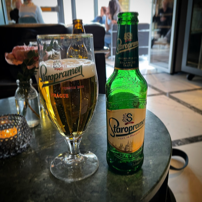 Ett glas och en flaska Staropramen öl på ett bord, användarens omdöme "tråkig öl" efter mässa.
