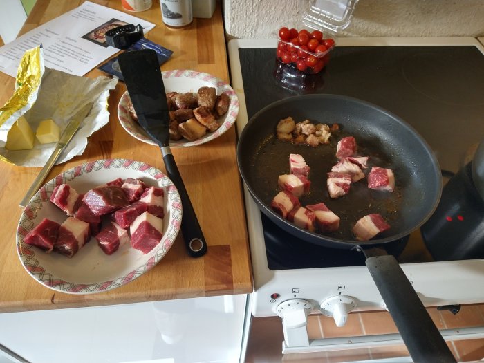 Bitar av nötbringa som bryns i en stekpanna, ingredienser och recept på köksbänk.