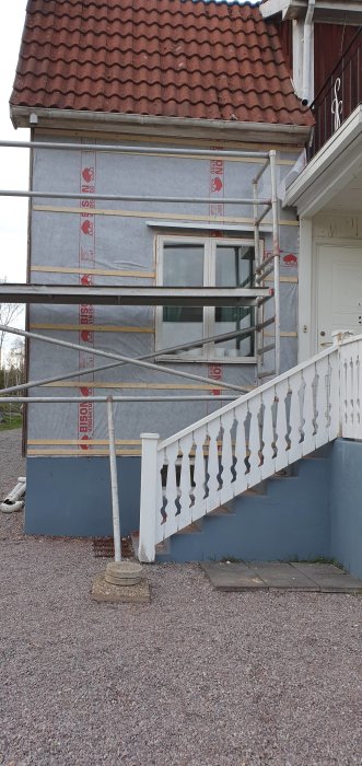 Husfasad under renovering med byggnadsställning och isoleringsmaterial synligt.