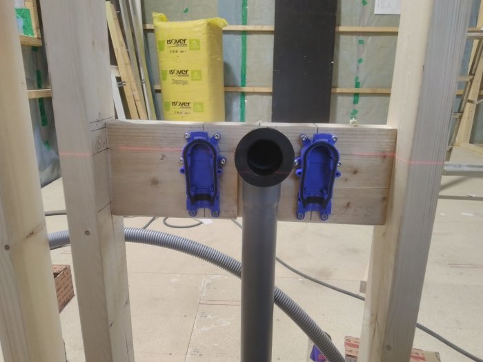 Installation av VVS med två blå väggfästen och ett centralt avloppsrör i ett pågående byggprojekt.