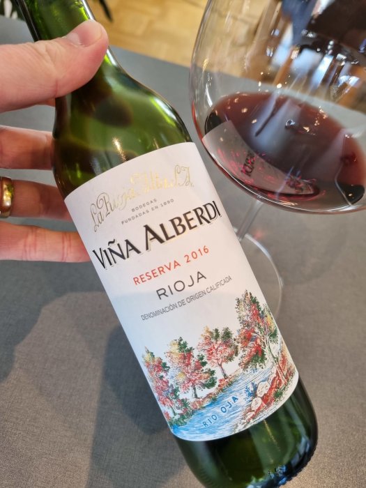 Halvflaska rioja Viña Alberdi Reserva 2016 hålls bredvid ett glas fyllt med rödvin.