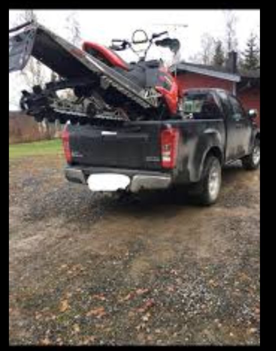 Pickup med öppen baklucka och en snöskoter delvis lastad ovanpå flaket, ytterligare släp ej synligt.