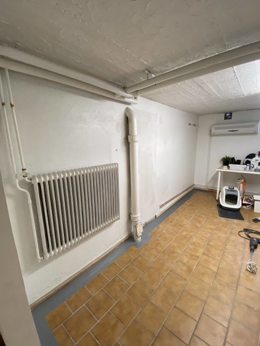 Ett förberett rum för målning med maskeringstejp, radiator och rör längs väggen.
