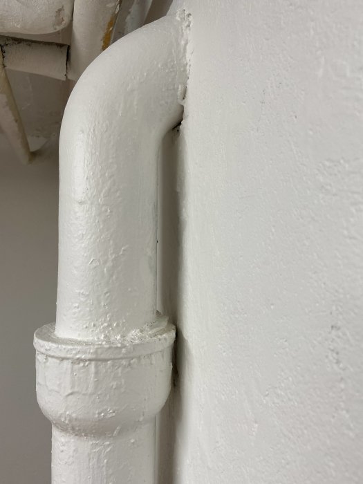 Nymålad vit rörinstallation mot en vit vägg, tecken på nyligen utförd renovering.