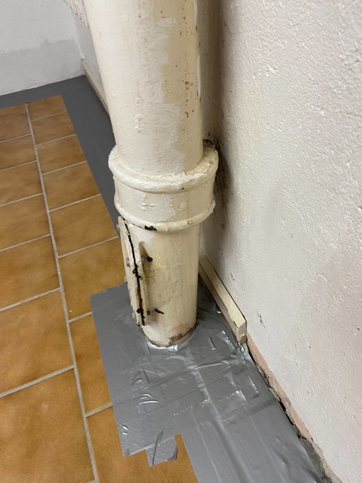Ett nymålat vitt rör längs en vägg, väl integrerat med målningen, över tejpbelagt golv.