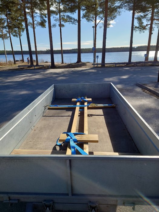 Tom släpvagn parkerad vid en sjö med träreglar säkrade med blå spännband.