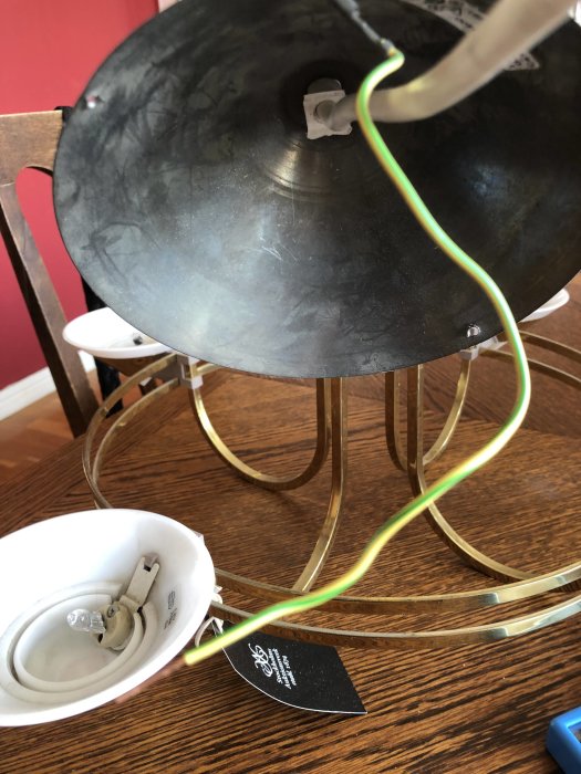Öppen taklampa med utsatt jordningssladd och synliga ledningsändar på ett träbord.