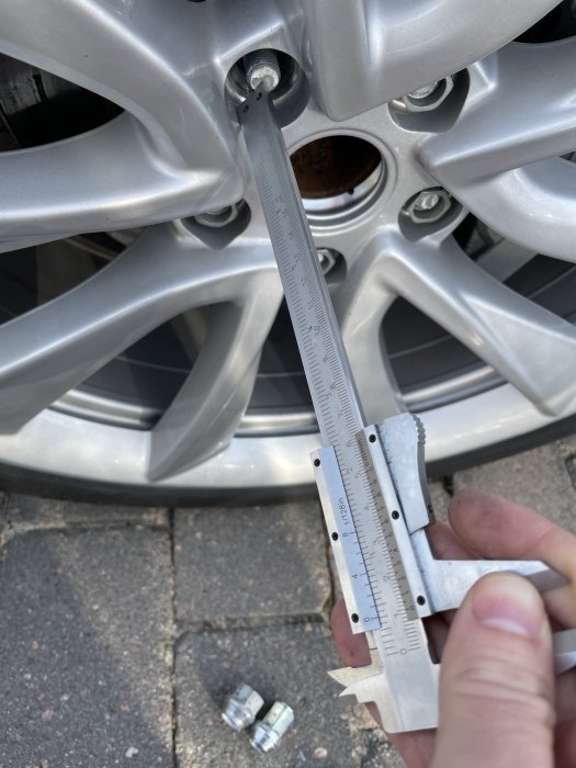 Skjutmått mäter utstick på en Tesla-fälg med fokuserad vy på ett hjulbultshål och borttagna muttrar på marken.