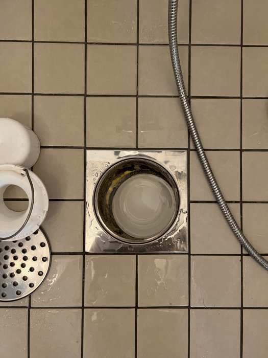 Golvbrunn i badrum där övre och nedre del inte är centrerade, med synlig gul poröst material.