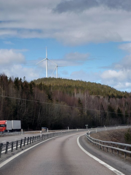 Vy över en landsväg med vindkraftverk i bakgrunden och en lastbil i rörelse.