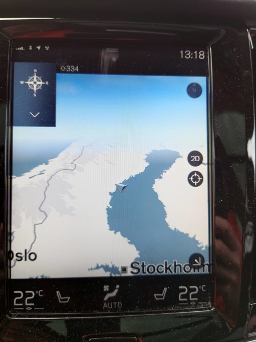 Bildskärm i bil visar GPS-karta över Skandinavien med markeringar för Oslo och Stockholm, klockan är 13:18, 22°C.