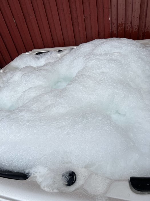 Spabad överfullt med skum och bubblor mot en röd trävägg.