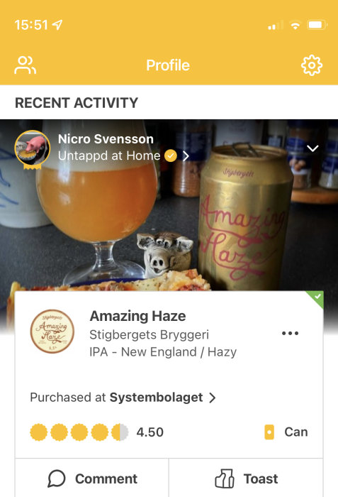 Ölglas fyllt med dimmig öl, Amazing Haze burk från Stigbergets Bryggeri, och en kommentarsgränssnitt från en app.