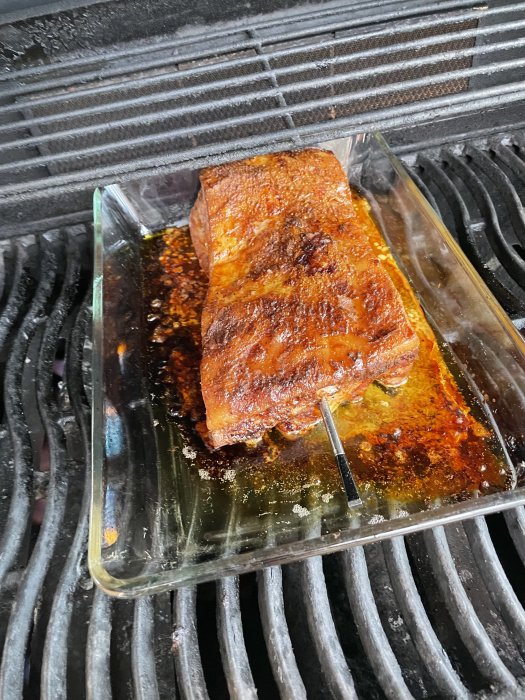 En fläsksida tillagas på lågtemperatur i en glasform på en grill.