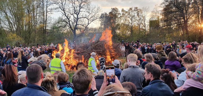 Folk samlade runt en stor brasa på kvällen, några fotograferar händelsen.