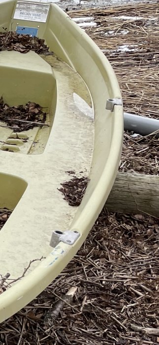 Grön båt utan årtullar med synliga fästen vid strandkanten.