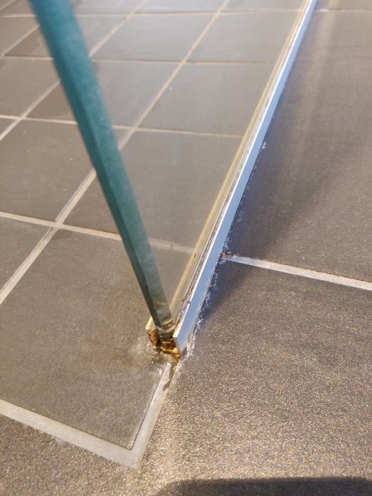 Svart klinkergolv med vita fläckar runt duschväggens nederkant där vatten har stått.