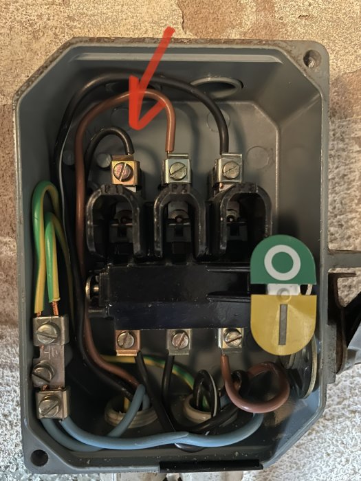 Elektriskt säkerhetsbrytarskåp med öppen kabelanslutning markerad av röd pil.
