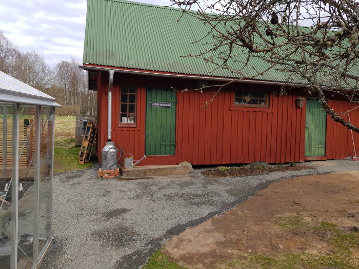 Ny anlagd gång med bergkross framför röd stuga som framtida uteplats, skottkärra synlig.