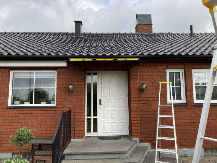 En nyinstallerad utelampa ovanför en vit dörr på ett tegelhus, med en stege som lutar mot väggen.