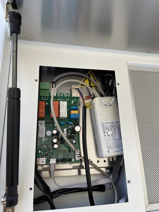 Öppen elektronikkåpa som visar ett styrkort med kondensatorer och anslutna kablar.