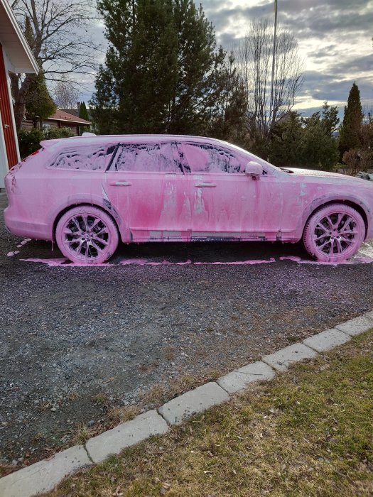 Bil täckt med rosa skummedel ståendes på en grusuppfart.