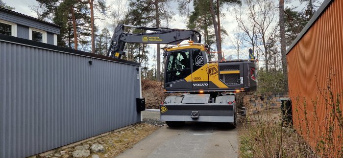 Grävmaskin från Marsta Förenade i arbete bredvid en nygjord husnära parkering med stenmur i bakgrunden.