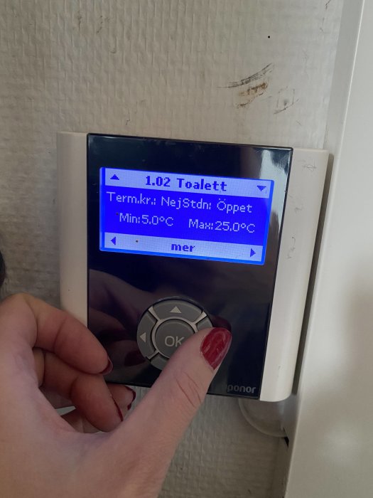 Hand justerar inställningar på en Uponor termostat för golvvärme som visar temperaturgränser.