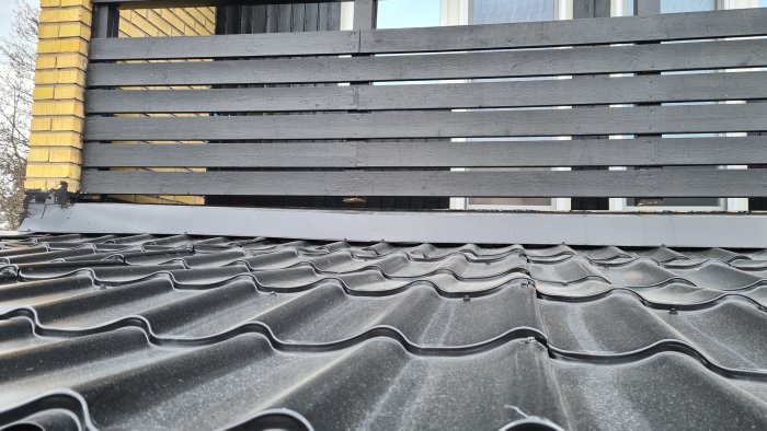 Svart staket ovanför mörkt tak, med vinklad plåt och tätningsmassa runt övergången för vattentätning.