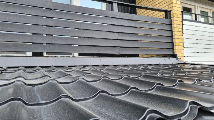 Takövergång med svartmålat staket och vattenavvisande plåt på ett takpannorliknande underlag.