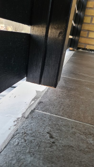 Detaljbild av uterum med svarta stolpar, klinkergolv och vit takfog vid övergången mellan platta och plåt.