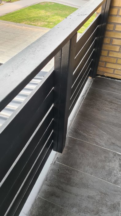 Svart balkongräcke med en övergångsplåt under klinkers på en balkong.