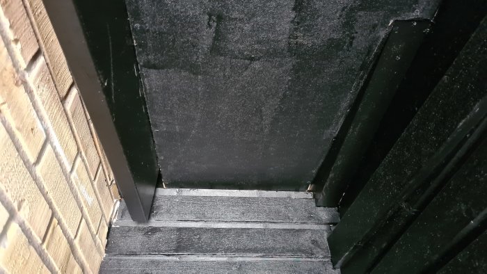 Svartmålad masonit och trappsteg med asfaltsklister och takfog applicerade för tätning, synliga efter reparationen.