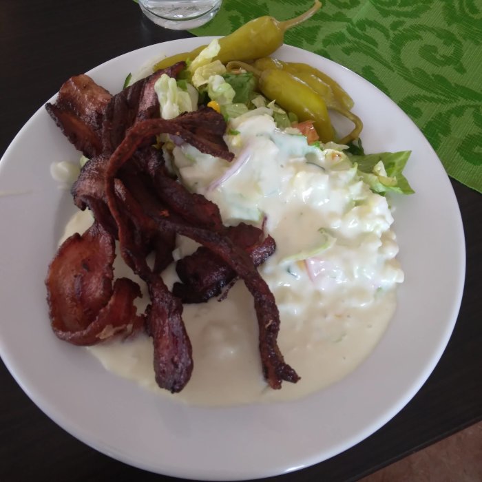 En tallrik med fläsk, löksås, sallad och inlagda gröna chilipeppar.