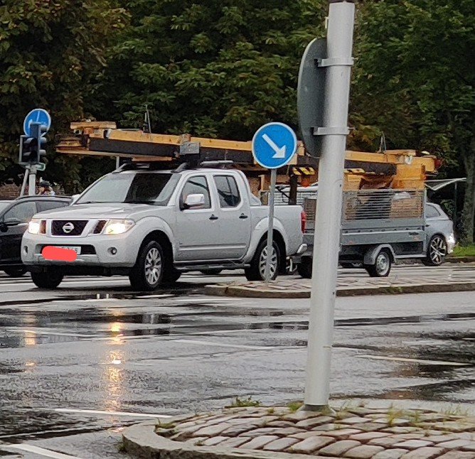 Svår lastad pickup med takbjälkar kopplad till en släpvagn i stadsmiljö.