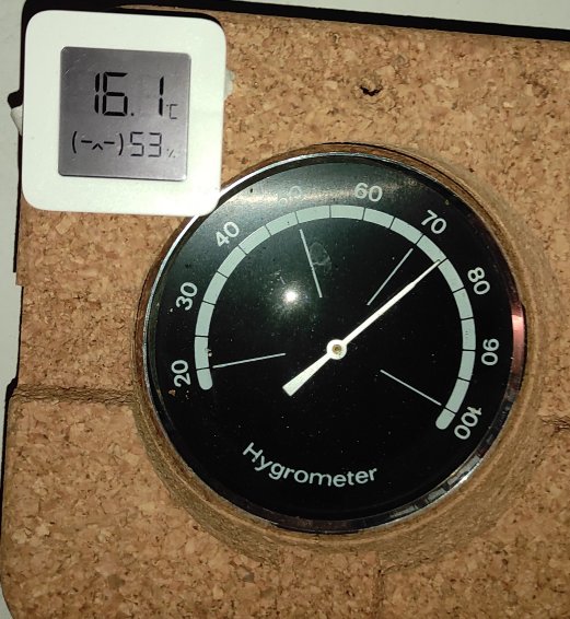 Digital och analog hygrometer som visar temperatur och luftfuktighet på en korkvägg.